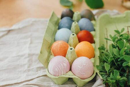 Modern yellow, pink, blue and grey easter eggs painted with organic onion, beets, red cabbage, carcade tea. Zero waste holiday. Natural dye easter eggs in carton tray on rustic table with flowersの写真素材