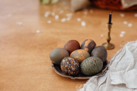 Modern Easter eggs on vintage plate on rustic wooden table with candle. Stylish grey stone and green...