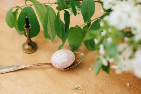 Modern Easter egg on spoon and spring flowers on rustic wooden table with candle. Stylish pastel pink Easter eggs painted in natural dye from beets. Happy Easterの写真素材