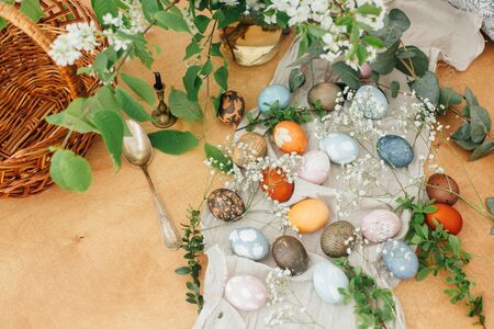 Easter eggs on rustic background with basket, candle, spring flowers and green branches. Stylish...