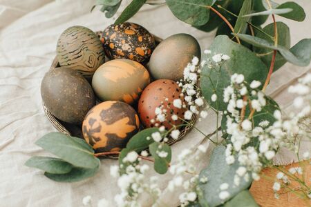 Modern Easter eggs with spring flowers and eucalyptus on rustic wooden table. Stylish grey stone and...
