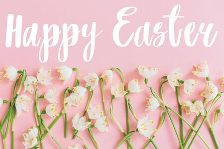 Happy Easter text on white spring flowers on pastel pink flat lay. Stylish easter creative  greeting card. Easter greetings. Banner with letteringの写真素材