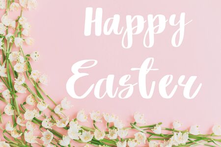 Happy Easter text on white spring flowers on pastel pink flat lay. Stylish easter creative  greeting...