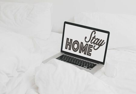 Stay home text on laptop screen and coffee cup on white soft bed.の写真素材