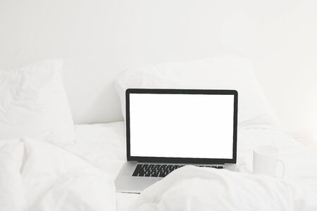 Laptop with blank white screen and coffee cup on white cozy bed, copy space. Shopping online from bed. Working online from home. Mockup. Freelance concept. Staying home. Blog templateの写真素材