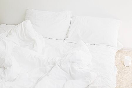 Cozy white bed in the morning. White sheets and pillow on bed in modern white room. Lazy days. Stay home. Comfortable place. Relax on weekend in hotel room. Messy bedの写真素材