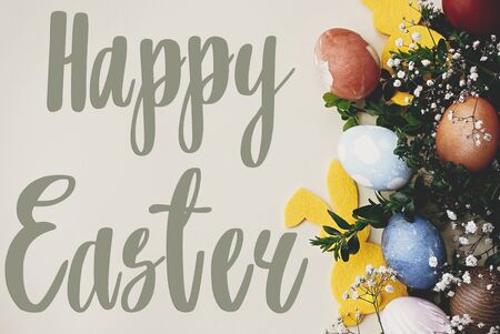 Happy Easter text. Easter greetings card. Stylish easter eggs, yellow bunny, spring flowers on...