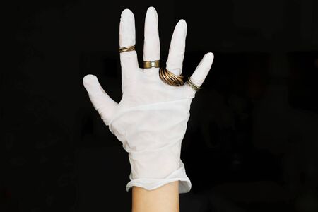 Hand in white medical glove with modern rings on fingers on black background. Fashion and...