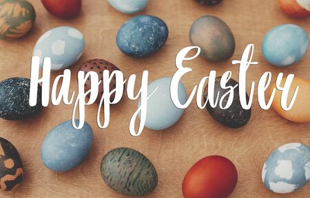 Happy Easter text. Easter greetings lettering. Modern Easter eggs on rustic wood. Stylish colorful eggs with modern ornaments. Greeting cardの写真素材