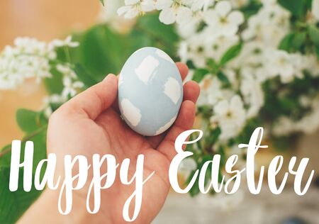 Happy Easter text. Easter greetings lettering. Hand holding modern Easter egg on background of...