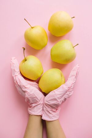 Hands in pink glove holding apples on pink background flat lay. Safe shopping in quarantine. Order food online with delivery and stay home. Prevention of virus epidemic. Stay safe.の写真素材