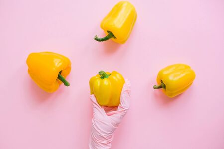 Hand in pink glove holding yellow pepper on pink background flat lay. Safe shopping in quarantine....