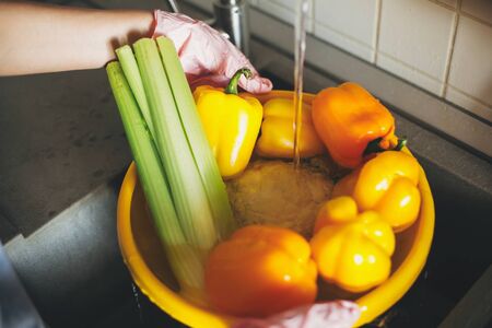 Washing vegetables. Hands in pink gloves washing vegetables in yellow bowl under water stream in sink. Woman  cleaning fresh pepper,celery, cauliflower, preparing for cookingの写真素材