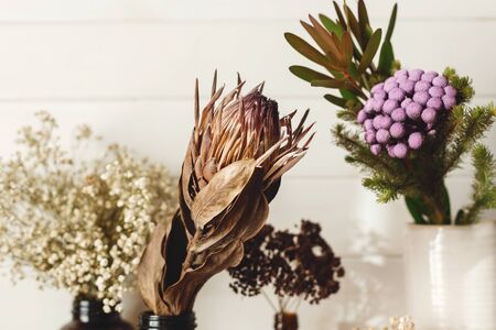 Dry protea flower, brunia, gypsophila and dried herbs in different brown glass bottles on wooden shelf in country home. Modern house decor. Stylish simple interior design elements. Rural houseの写真素材
