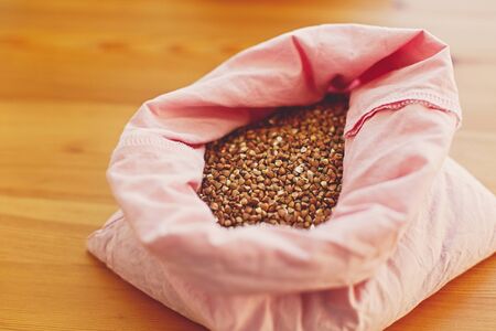 Zero waste shopping. Organic buckwheat grain in reusable bag close up. Groceries in reusable textile bags on wooden table. Plastic free delivery from bulk store.  Ban plasticの写真素材