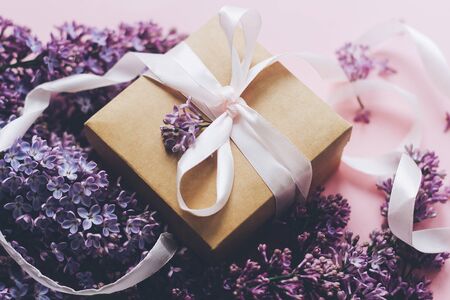 Lilac flowers and gift box on pink background. Stylish floral greeting card. Purple lilac flowers bouquet, craft present box with ribbon on pink paper. Happy mothers dayの写真素材