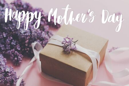 Happy Mother's day text and lilac flowers, gift box on pink background. Stylish purple lilac flowers...