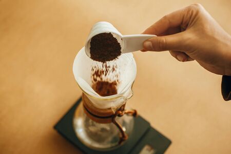 Hands pouring grounded coffee in filter pour over on glass kettle on scaleの写真素材