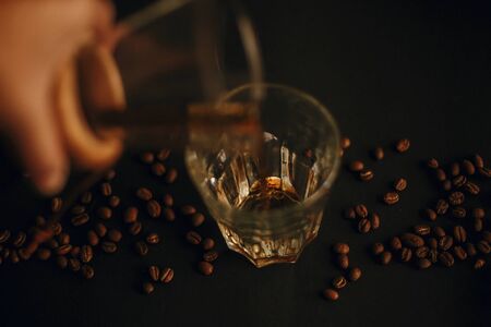 Hand pouring fresh coffee in glass cup with coffee beans on blackの写真素材