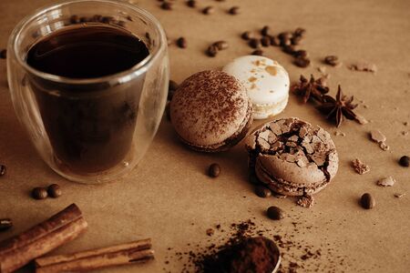 Coffee moody image. Glass cup with fresh coffee and roasted beans,ground coffee on spoon, macarons, chocolate, cinnamon on brown background. Coffee brewingの写真素材