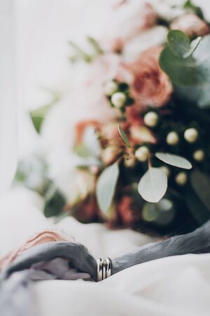 Silver wedding rings and engagement diamond ring on grey fabric, creative macro view. Marriage and divorce concept. Stylish wedding rings on background of modern wedding bouquetの写真素材
