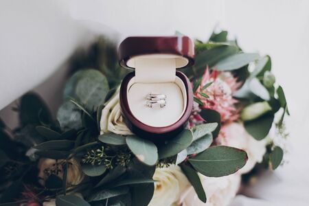 Marriage and divorce concept. Silver wedding rings and stylish modern wedding bouquet of pink roses and green eucalyptus on white soft tulle. Wedding arrangementsの写真素材