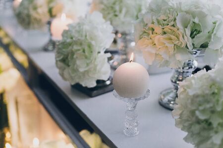 Modern decor at evening wedding reception in restaurant. Stylish white hydrangea and modern white candles with light at tables. Luxury cateringの写真素材