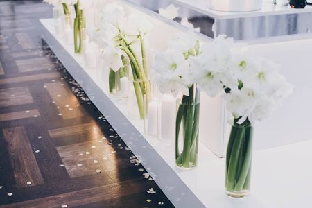 Modern decor at evening wedding reception in restaurant. Stylish white lily flowers and modern white candles with light at tables. Luxury cateringの写真素材