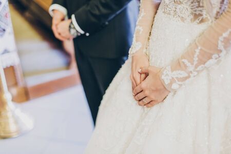 Bride and groom hands close up during holy matrimony in church. Wedding spiritual ceremony. Bride hands on luxury gown. Wedding couple prayingの写真素材