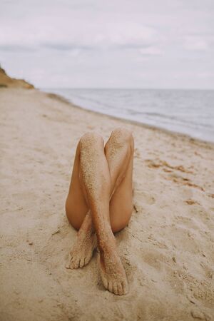 Tanned legs of a girl on beach with sand on smooth skin. Beautiful authentic and unusual image. Young woman relaxing on seashore with sandy legs. Summer vacation. Feet careの写真素材