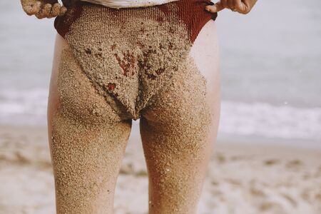 Young woman butt and legs in sand close up on beach. Happy wet girl with sandy swimsuit and legs...