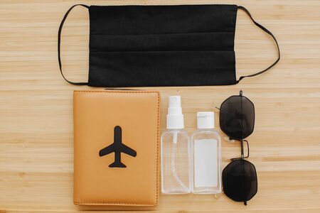 Coronavirus summer 2020 flat lay. Black face mask, gloves, antiseptic and disinfectant, passport, sunglasses  on wooden background. Safe travel in 2020, new normalの写真素材