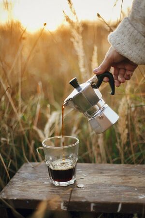 Hipster pouring fresh hot coffee from geyser coffee maker into glass cup in sunny warm light in rural countryside herbs.の写真素材