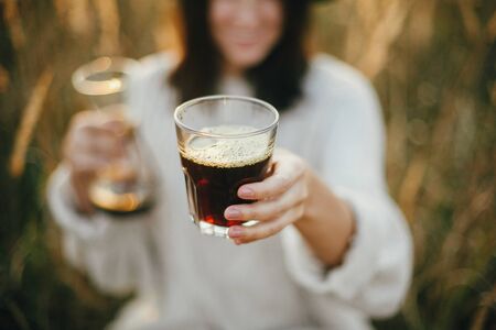 Hipster woman holding hot coffee in glass cup on background of rural herbs in sunset. Alternative coffee brewing outdoors in sunny light. Atmospheric rustic moment. Travel and Wanderlustの写真素材