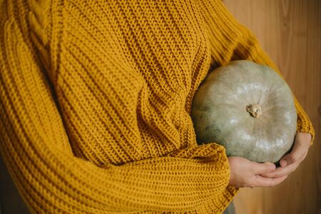Girl in yellow knitted sweater holding  pumpkin on background of rustic wooden wall. Autumn harvest season in countryside. Happy Thanksgivingの写真素材