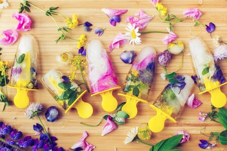 Floral Ice Pops flat lay. Colorful wildflowers in frozen ice cubes and fresh summer flowers on...