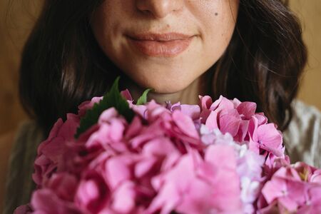 Young woman smelling beautiful hydrangea bouquet on background of  rustic wood. Girl holding pink and purple hydrangea flowers, cropped view. Beautiful scentの写真素材