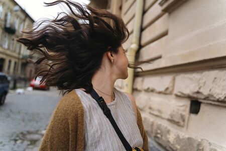 Happy stylish hipster girl waving curly hair and walking in city street. Young woman in casual fashionable outfit having fun in european city. Moment of happinessの写真素材