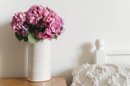 Hydrangea bouquet in vase white pillow on bed on background of white wall with copy space. Beautiful...