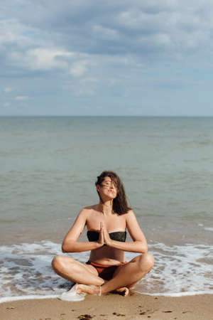 Mental health and self care concept. Young beautiful woman practicing yoga on the beach, sitting on...