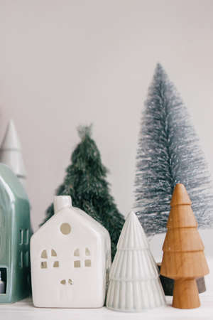 Christmas little houses and trees on white background. Festive modern decor. Happy holidays. Miniature cozy village, ceramic houses, wooden and handmade christmas trees. Seasons greetingの写真素材