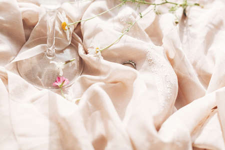 Daisy flowers, white wildflowers, rings at wineglass stem on background of soft beige fabric. Tender floral aesthetic. Creative summer image. Bohemian moodの写真素材