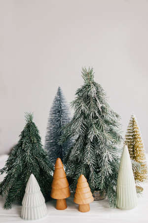 Christmas trees on white background. Festive modern decor. Happy holidays. Miniature ceramic,wooden, snowy and handmade pine trees. Season greeting. Merry Christmas.の写真素材