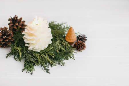 Christmas pine cone candle and tree in rustic christmas wreath on white wood. Small pine tree and modern wreath from white cedar and pine cones. Festive modern decor. Copy spaceの写真素材