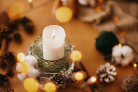 Christmas candle in rustic holder made of branches, cotton, anise and pine cones on wooden table in festive lights bokeh. Making rustic christmas candle decor. Holiday workshopの写真素材