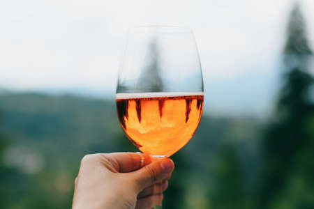 Hand holding delicious orange cocktail on background of mountains, summer vacation and resort. Woman cheering with aperol drink, celebrating outdoorsの写真素材