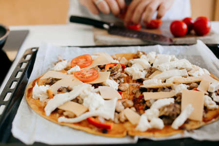 Home made pizza. Person putting cheese, tomato, mozzarella on dough with ketchup, chicken and...