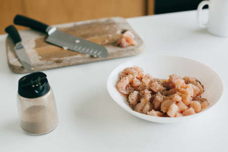 Marinate slice of chicken fillet in spices and knife on wooden board on modern white kitchen....