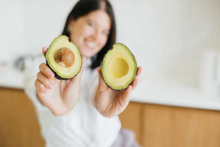 Healthy food concept. Young happy woman showing half of perfectly ripe avocado in hands and smiling...