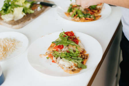 Slice of delicious pizza with mushrooms, tomato, arugula and cheese. Home cooking concept. Hands...